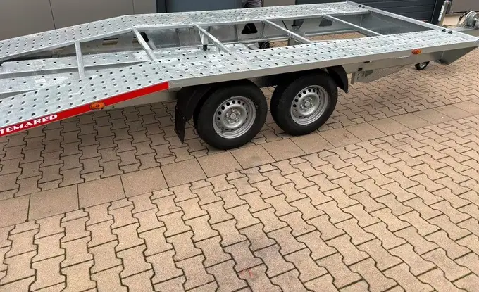 Derselbe Anhänger von der Seite: zwei Achsen mit Rädern und lange, flache Ladefläche