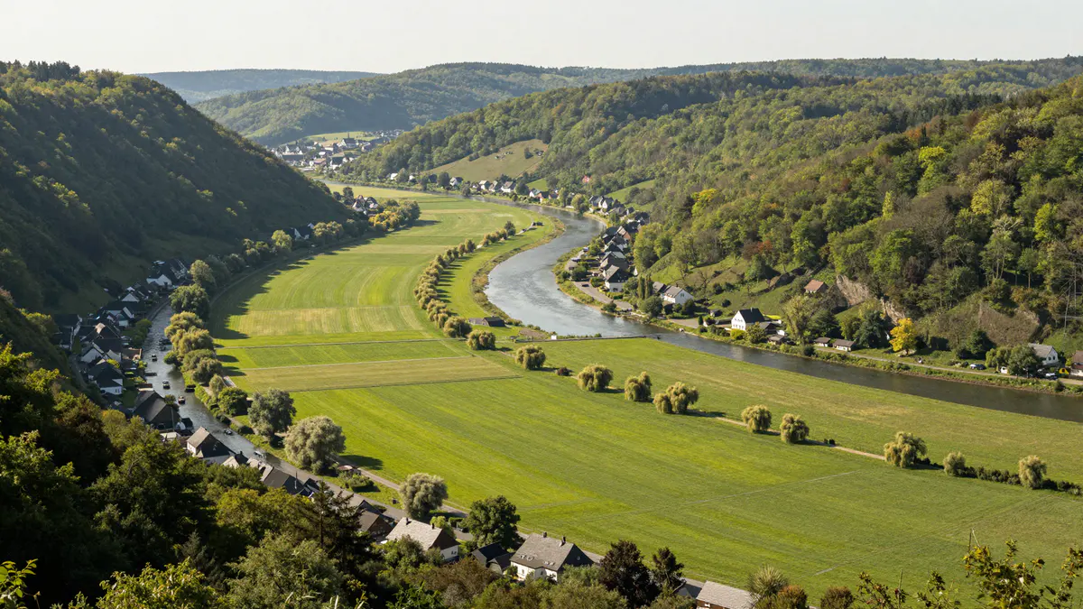 Illustration: Blick von oben in ein grünes Flusstal mit Flussschleife, Auenwiesen, kleinen Dörfern und bewaldeten Hängen