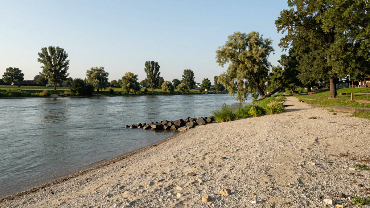 Illustration: Kiesstrand an einem breiten Fluss mit dunkler Steinbuhne, Weiden und Pappeln im Abendlicht
