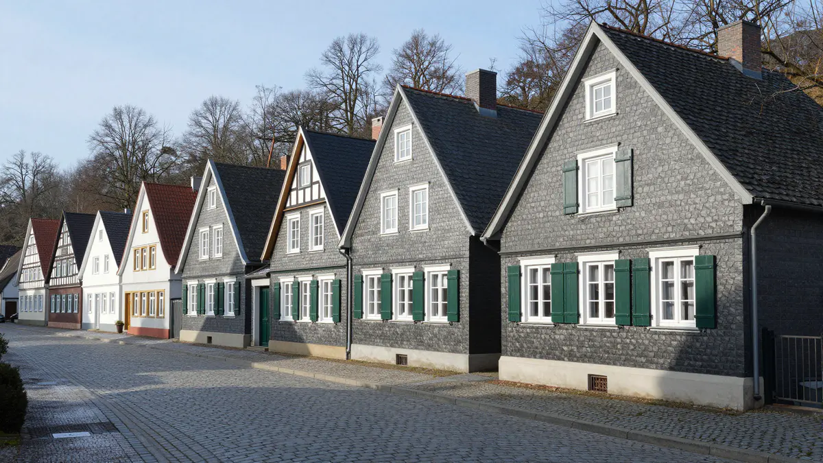 Illustration: Gepflasterte Altstadtstraße mit schieferverkleideten Giebelhäusern, weißen Fenstern und grünen Fensterläden im Winter