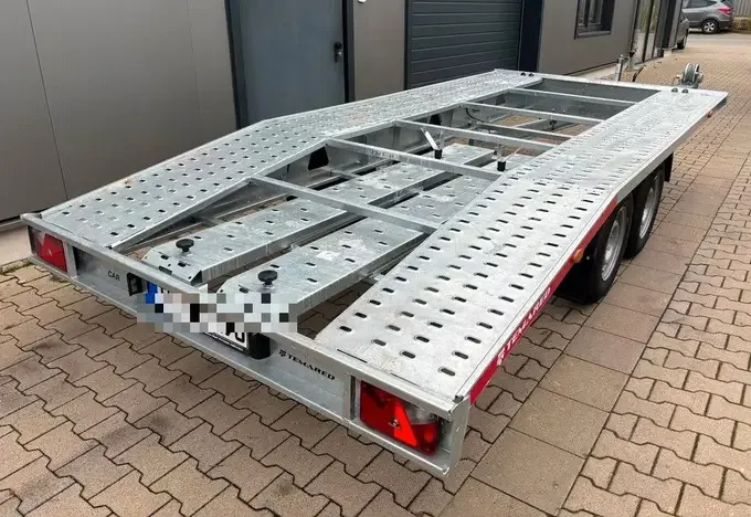 Autotransporter-Anhänger mit Ladefläche aus verzinktem Stahl, von hinten schräg fotografiert, auf einem gepflasterten Hof
