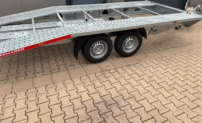 Derselbe Anhänger von der Seite: zwei Achsen mit Rädern und lange, flache Ladefläche
